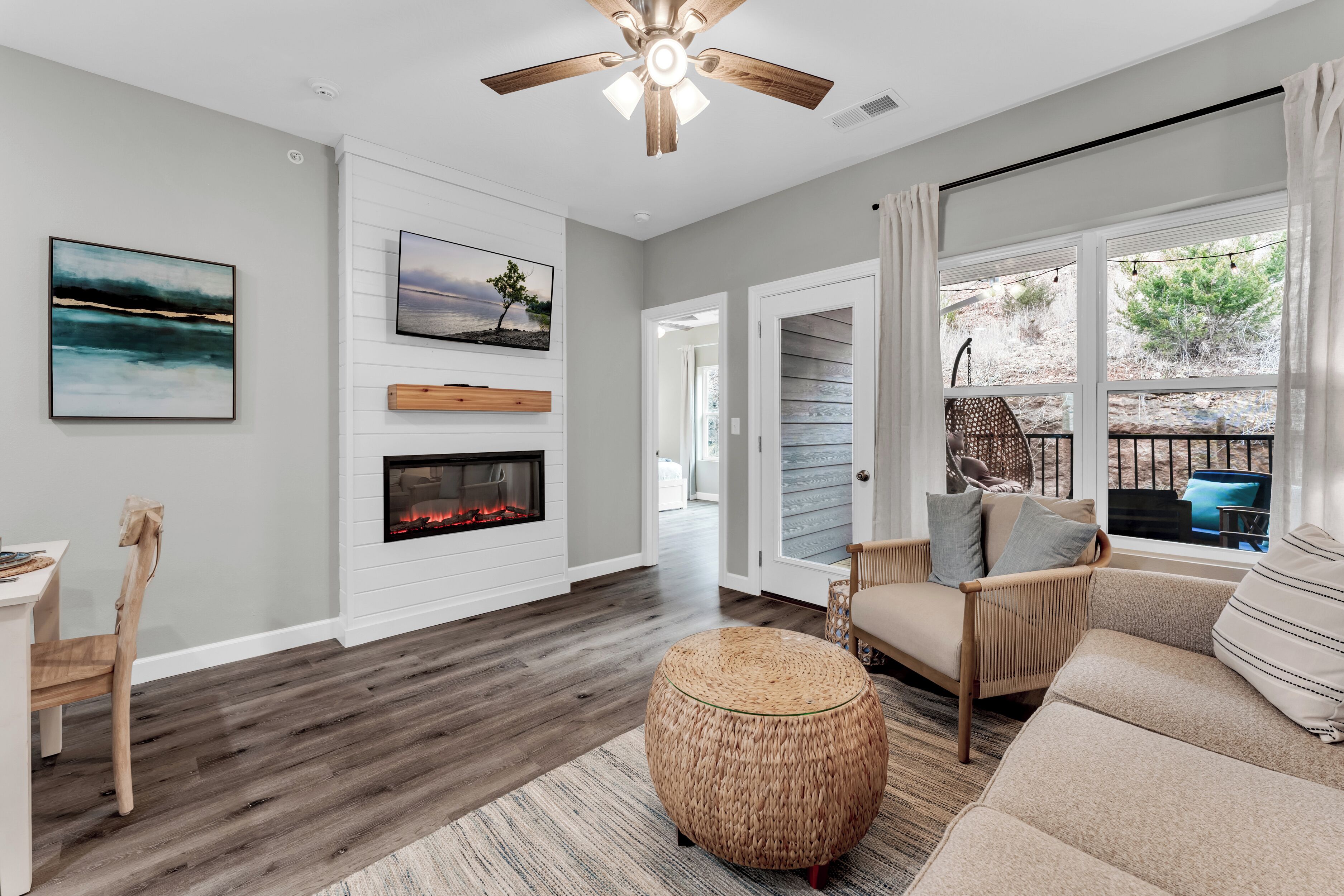 A living room with a fireplace, a ceiling fan, and a large window with curtains.