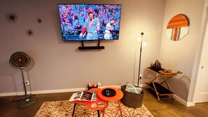 A living room with a flat-screen TV mounted on the wall, a standing fan, a small table with magazines, and a decorative lamp. - Spacious private whole guest house in NE Portland! (Portland)