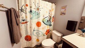 A bathroom with a space-themed shower curtain, a toilet, a towel rack, and a wall-mounted soap dispenser. - Spacious private whole guest house in NE Portland! (Portland)