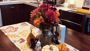 A dining table with a floral tablecloth, a vase of flowers, and decorative pumpkins. - Spacious private whole guest house in NE Portland! (Portland)
