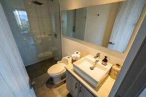 Ein modernes Badezimmer mit einer Duschkabine aus Glas, einer Toilette, einem Waschbecken mit Spiegel darüber und einem Schrank mit Pflegeprodukten.