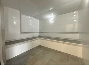 Ein Badezimmer mit weißen Wänden, einem grauen Fliesenboden und einem Spiegel mit grauem Rahmen.