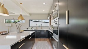 Une cuisine moderne avec des meubles de couleur sombre, un plan de travail blanc et des luminaires suspendus dorés.
