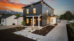 Une maison moderne à deux étages, dotée d’une façade sombre, de grandes fenêtres et d’un jardin bien entretenu.