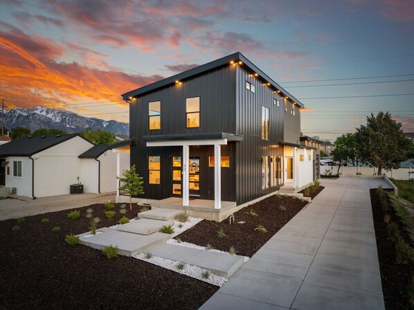 Une maison moderne à deux étages, dotée d’une façade sombre, de grandes fenêtres et d’un jardin bien entretenu.