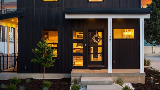 Une maison moderne à deux étages, dotée d’une façade sombre, de grandes fenêtres et d’une porte d’entrée ornée d’une guirlande.