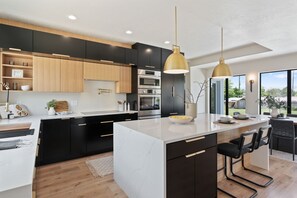 Une cuisine moderne avec des meubles de rangement noirs et en bois, un grand îlot central et des luminaires suspendus.