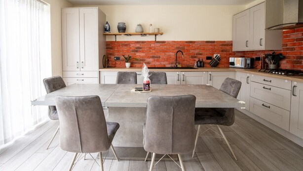 Une cuisine moderne avec un mur de fond en briques, des armoires blanches et une table à manger avec des chaises.