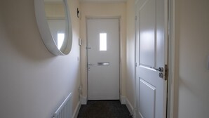 Un couloir avec une porte blanche, une petite fenêtre et un miroir accroché au mur.