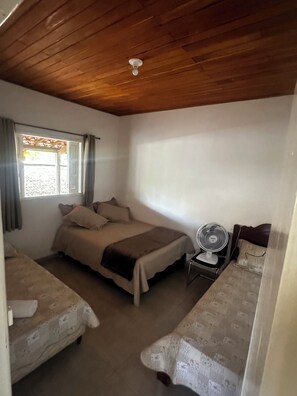 A room with two beds, a ceiling fan, and a window with curtains.