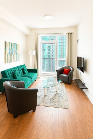 A modern living room with a green sofa, a black armchair, a glass coffee table, and a television on a stand. - Luxury 1-Bedroom- Yonge & Sheppard-Direct Subway (Toronto)