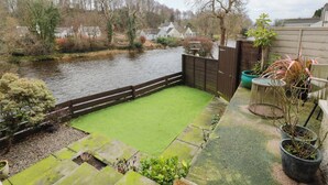 A backyard with a green lawn, a wooden fence, and a river in the background. - 7 Brewery Pool (Newton Stewart)