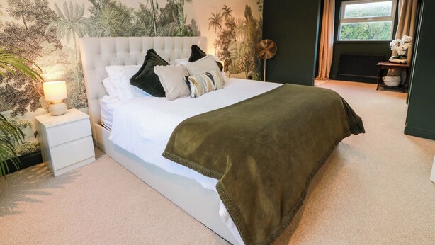 A bedroom with a large bed, a nightstand, a wall-mounted fan, and a window with curtains. - 7 Brewery Pool (Newton Stewart)