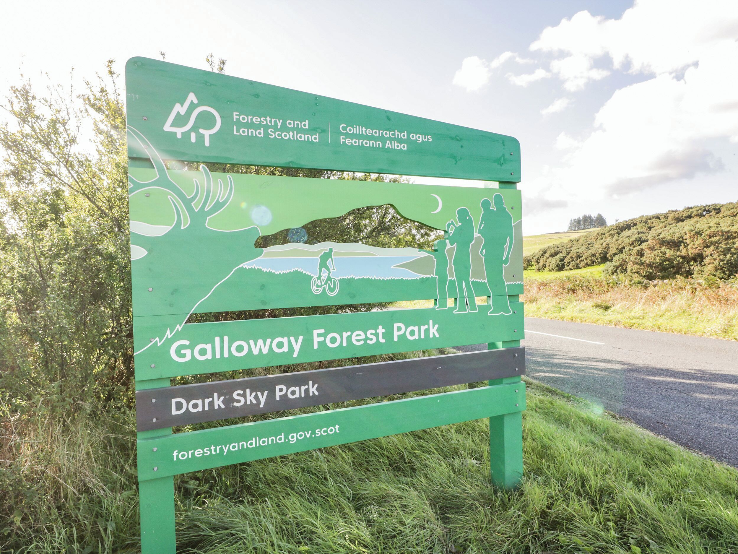 A sign for Galloway Forest Park with a silhouette of a person on a bike, a child, and an adult.
