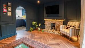A modern living room with a fireplace, a television mounted on the wall, and a seating area with a striped armchair. - 7 Brewery Pool (Newton Stewart)