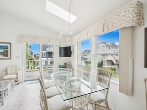 A spacious dining area with a glass table and wicker chairs, a chandelier, and a view of neighboring houses. - Spacious Bethany Beach Home w/ Deck (Bethany Beach)