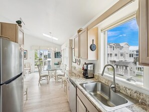 A modern kitchen with a stainless steel refrigerator, granite countertop, and a large window with a view of houses. - Spacious Bethany Beach Home w/ Deck (Bethany Beach)