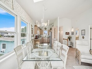 A dining area with a glass table and white chairs, a kitchen with modern appliances, and a view of a body of water through large windows. - Spacious Bethany Beach Home w/ Deck (Bethany Beach)