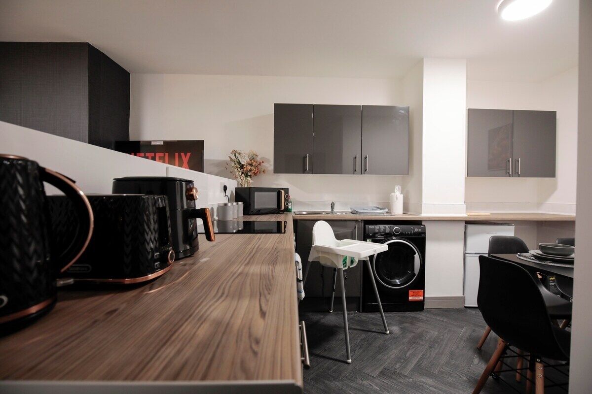 Een moderne keuken met donkere kastjes, een houten aanrecht, een magnetron, een spoelbak en een wasmachine.