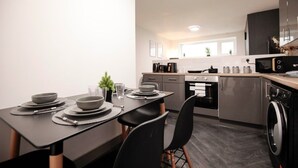 Une cuisine moderne avec une table à manger pour deux personnes, des appareils en acier inoxydable et une fenêtre laissant entrer la lumière naturelle.