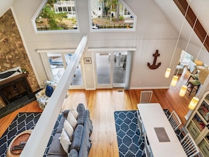 A spacious loft-style living area with a high ceiling, a fireplace, a dining area, and a view of the outdoors. - Waterfront 4BR House w/ Private Dock | Nr Beaches! (Bethany Beach)