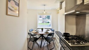 A modern kitchen with a gas stove, a dining table with chairs, and a window with a view of a house. - Littlebrooke House | Bolton | Free Parking (Bolton)
