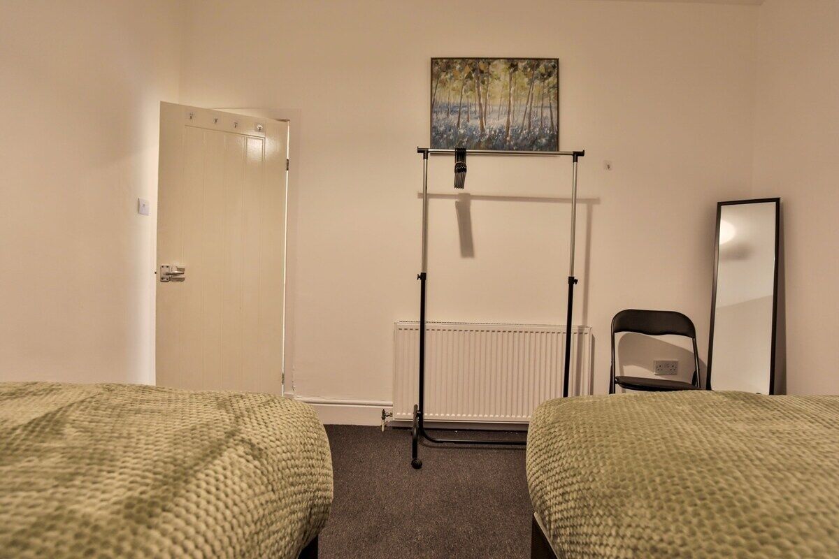 Une chambre d’hôtel avec deux lits, un radiateur, une chaise, un tableau au mur et une porte.