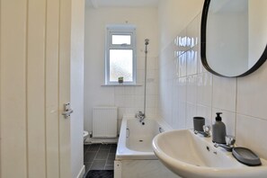 A bathroom with a bathtub, a sink, a mirror, and a window.