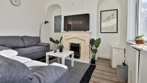 A modern living room with a grey sofa, a white coffee table, a fireplace, and a TV mounted above it. - Athol House, 2BR near Trafford Park, Free Parking (Salford)