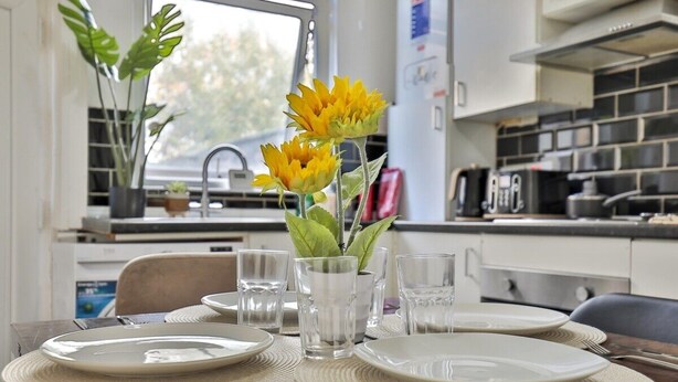 A dining table set with plates, glasses, and cutlery, with a vase of sunflowers in the center. - Athol House, 2BR near Trafford Park, Free Parking (Salford)
