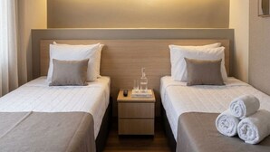 Une chambre d’hôtel avec deux lits, une table de chevet et une petite table sur laquelle se trouvent une bouteille et des verres.