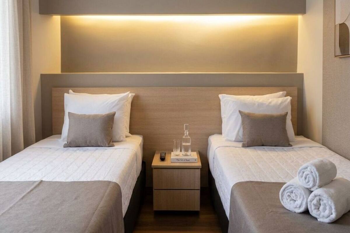 Ein Hotelzimmer mit zwei Betten, einem Nachttisch und einem kleinen Tisch mit einer Flasche und Gläsern.