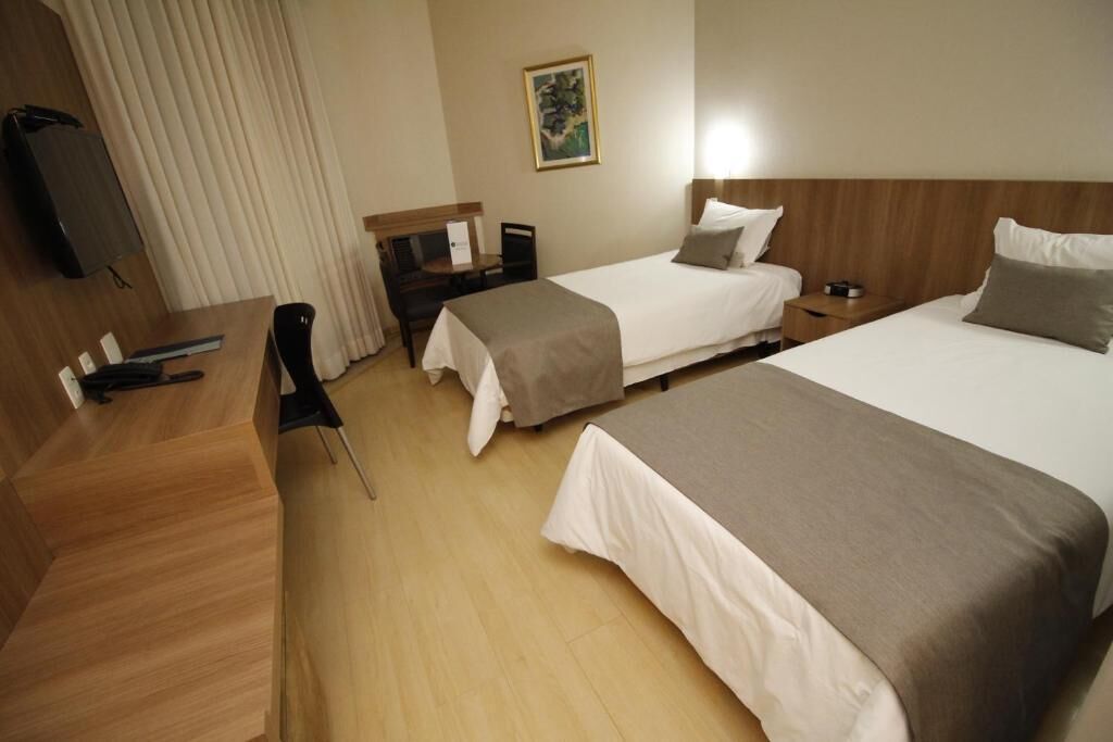 A hotel room with two beds, a desk, a chair, a TV, and a painting on the wall.