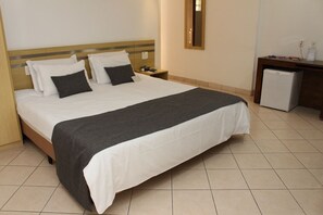 A hotel room with a bed, bedside table, nightstand, and a small refrigerator. - Actuall Convention Hotel  (Contagem)