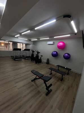 Een sportschool met trainingsapparatuur, een bank en een wandairconditioner.