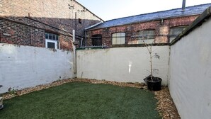 Ein durch eine Zäunung abgegrenzter Garten mit Rasen, ein Backsteinhaus und ein Blumentopf.