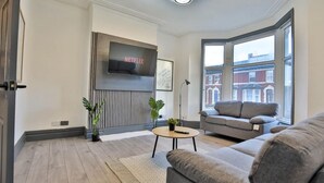A modern living room with a grey sofa, a round coffee table, and a flat-screen TV mounted on the wall. - Chesterfield House, 7BR, Blackpool (Blackpool)