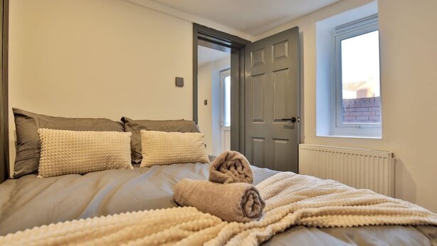 A bedroom with a large bed, two pillows, a rolled towel, a window, and a door. - Chesterfield House, 7BR, Blackpool (Blackpool)