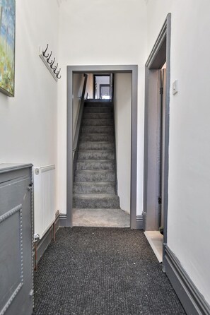 A narrow hallway with a carpeted staircase leading to a door. - Chesterfield House, 7BR, Blackpool (Blackpool)
