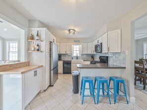 A modern kitchen with white cabinets, a central island with stools, a microwave, and a trash can. - 4-Bedroom House Near Beaches w/ Pool & Fire Pit (North Cape May)
