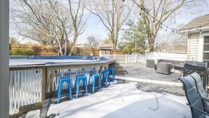 Ein Garten mit Whirlpool, blauen Stühlen, einem Grill und einer Holzterrasse.