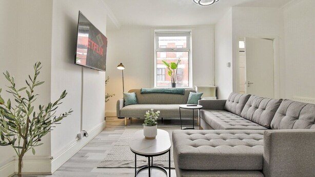 Una sala de estar moderna con un sofá seccional gris, una mesita redonda y un televisor montado en la pared.