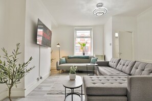 Una sala de estar moderna con un sofá seccional gris, una mesita redonda y un televisor montado en la pared.