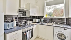 Una cocina moderna con armarios blancos, salpicadero de baldosas negras, lavadora integrada y ventana con vistas a árboles.