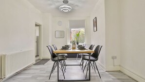 Un comedor con una mesa rectangular, sillas negras, una lámpara en el techo, una ventana y un radiador.