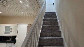Eine Treppe führt zu einer Tür, links daneben befindet sich eine Küche.