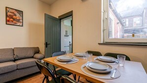 A dining area with a wooden table set for four, a grey sofa, and a window with a view of a building.