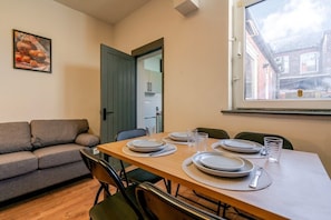 Un coin repas avec une table en bois dressée pour quatre personnes, un canapé gris et une fenêtre donnant sur un immeuble.