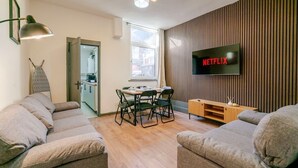 A modern living room with a sofa, a dining table with chairs, a TV mounted on the wall, and a wooden cabinet.