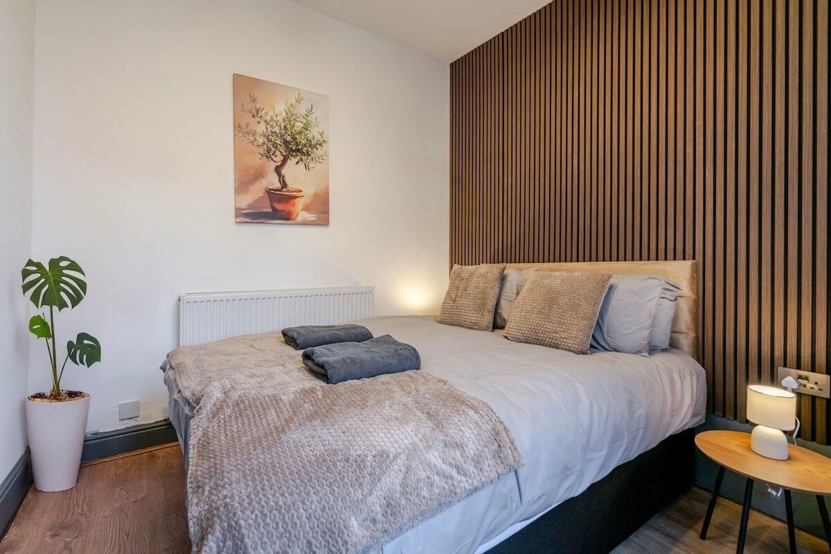 Une chambre moderne avec un lit, une plante en pot, un radiateur et un mur recouvert de panneaux en bois.